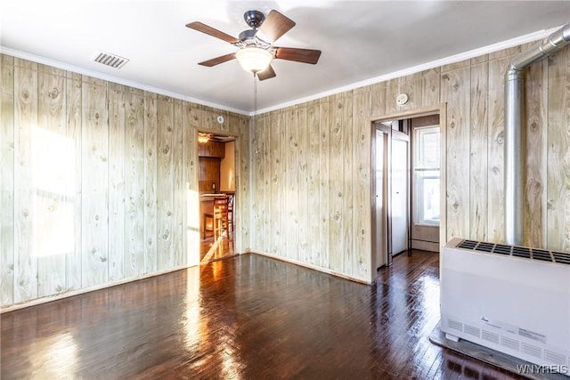 empty room featuring heating unit, crown molding, dark wood-type flooring, and ceiling fan