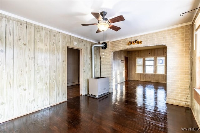 spare room featuring crown molding, brick wall, dark hardwood / wood-style flooring, and a wood stove