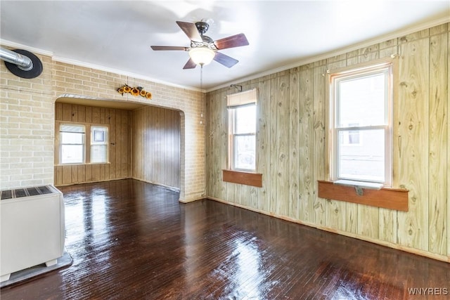 unfurnished room with ceiling fan, heating unit, wood-type flooring, ornamental molding, and brick wall