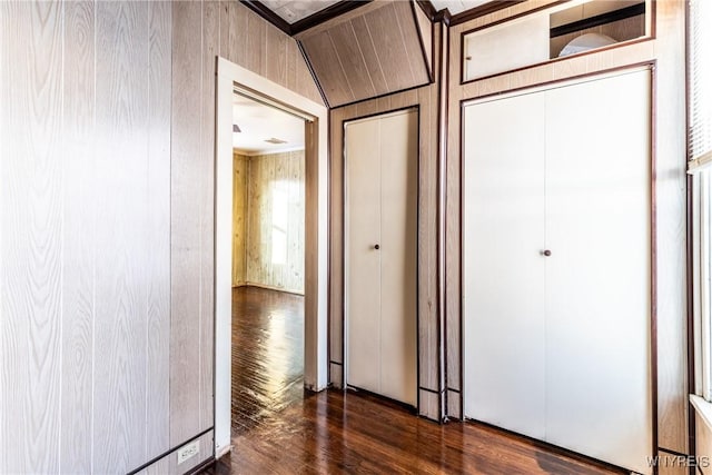 unfurnished bedroom featuring dark wood-type flooring, lofted ceiling, wooden walls, and a closet