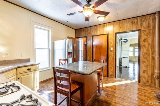 kitchen with wooden walls, stainless steel fridge, a kitchen bar, ceiling fan, and light wood-type flooring