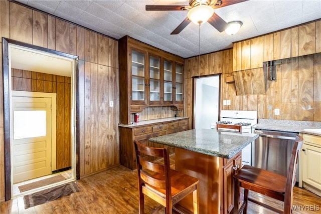 kitchen featuring ceiling fan, wooden walls, a kitchen island, stainless steel dishwasher, and light wood-type flooring