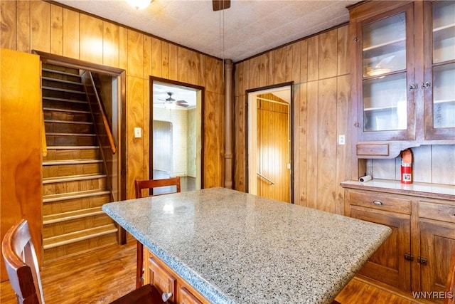 kitchen featuring light hardwood / wood-style flooring, ceiling fan, light stone counters, a kitchen bar, and wood walls