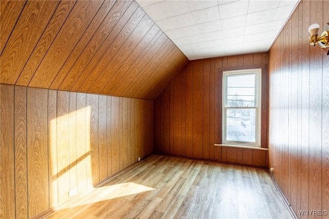 additional living space with light hardwood / wood-style floors, vaulted ceiling, and wood walls