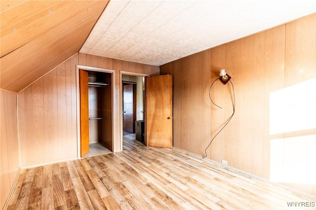 unfurnished bedroom featuring lofted ceiling, light wood-type flooring, a closet, and wood walls