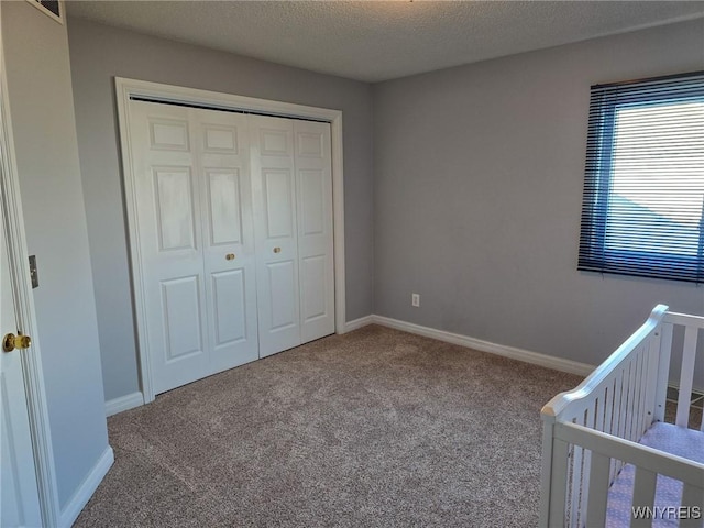 unfurnished bedroom featuring a crib, carpet, a textured ceiling, and a closet