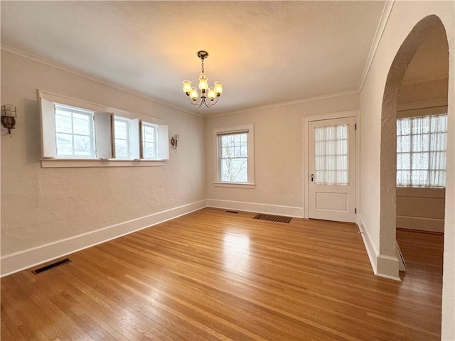 empty room with wood-type flooring, crown molding, and an inviting chandelier