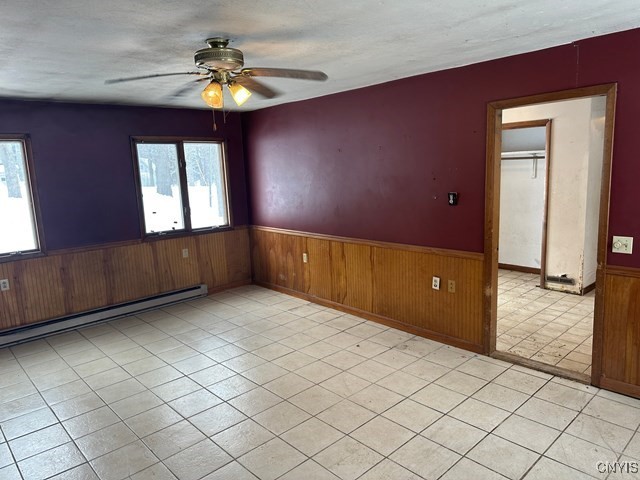 spare room with ceiling fan, a baseboard radiator, and wood walls