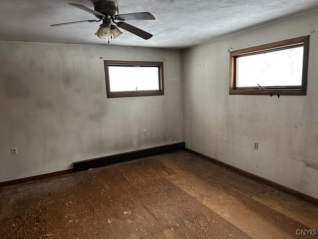 empty room featuring ceiling fan, plenty of natural light, a textured ceiling, and baseboard heating