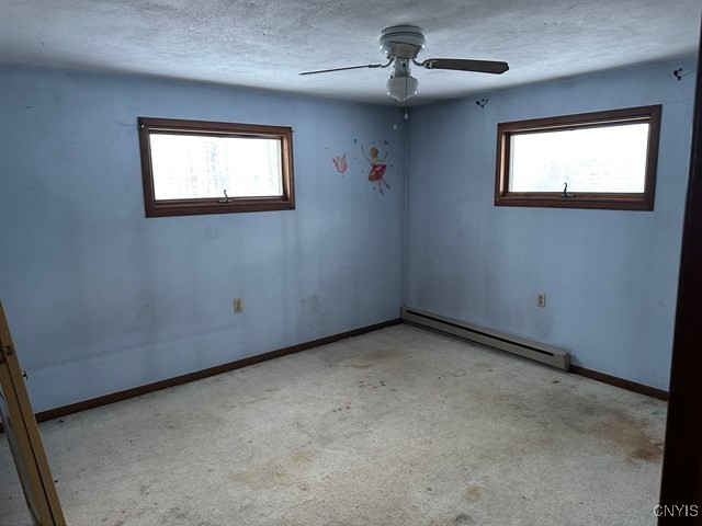 carpeted spare room featuring a healthy amount of sunlight, a baseboard heating unit, ceiling fan, and a textured ceiling