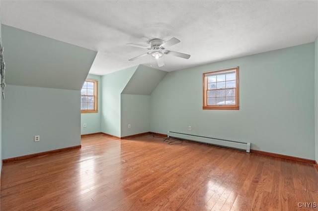 additional living space featuring ceiling fan, lofted ceiling, light wood-type flooring, and a baseboard heating unit