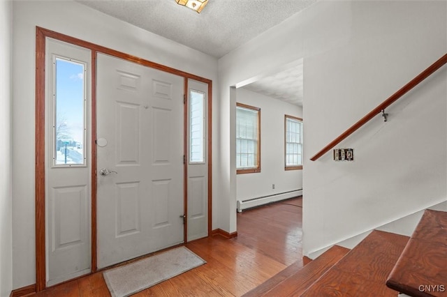 foyer featuring a baseboard radiator, plenty of natural light, a textured ceiling, and light wood-type flooring