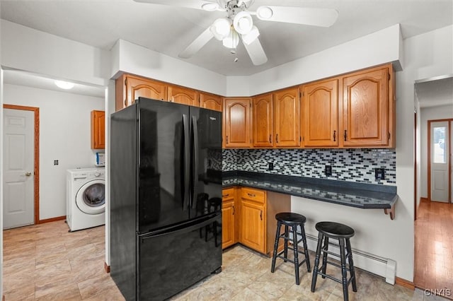 kitchen featuring black refrigerator, a baseboard heating unit, a kitchen bar, washer / clothes dryer, and decorative backsplash