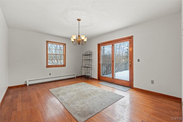 spare room featuring wood-type flooring, a baseboard heating unit, a wealth of natural light, and a notable chandelier