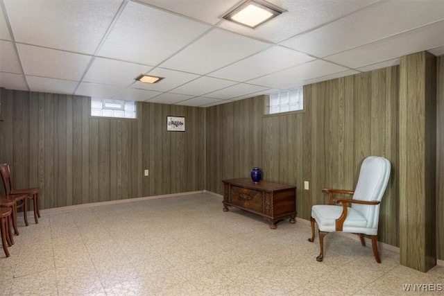 sitting room with wood walls, plenty of natural light, and a drop ceiling