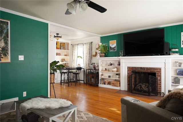 living room featuring crown molding, ceiling fan, a fireplace, and hardwood / wood-style floors