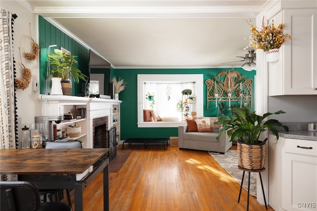 interior space featuring crown molding, ceiling fan, a brick fireplace, and light hardwood / wood-style flooring