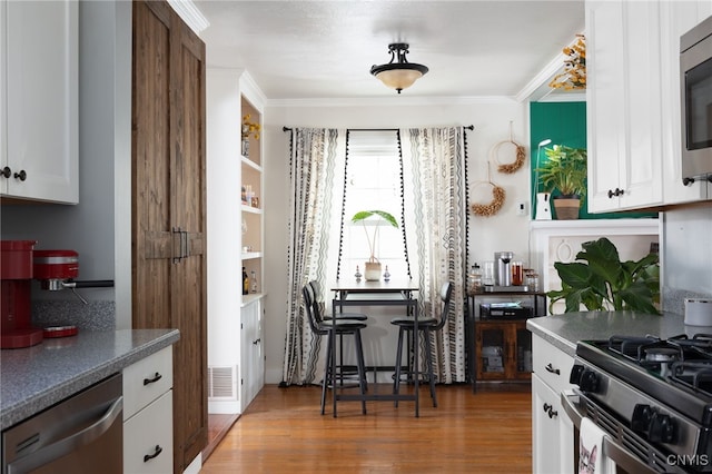 kitchen featuring stainless steel appliances, white cabinetry, ornamental molding, and dark wood-type flooring