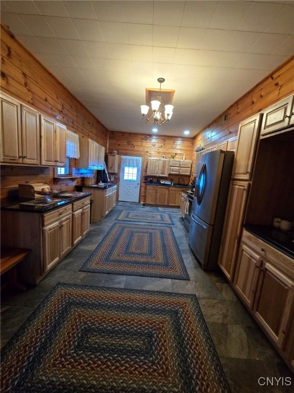 kitchen featuring stainless steel refrigerator, a notable chandelier, hanging light fixtures, and wood walls