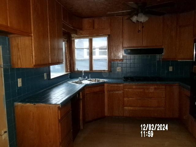 kitchen with tasteful backsplash, range hood, sink, and black cooktop