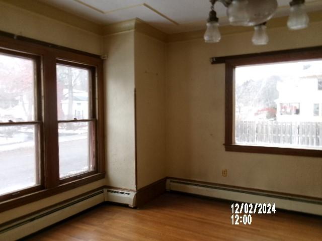 unfurnished room featuring a baseboard heating unit and hardwood / wood-style floors