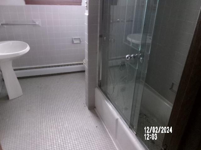 bathroom with baseboard heating, shower / bath combination with glass door, tile patterned flooring, and tile walls