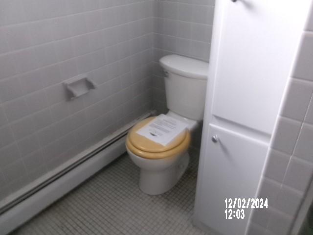 bathroom with tile walls, baseboard heating, and toilet