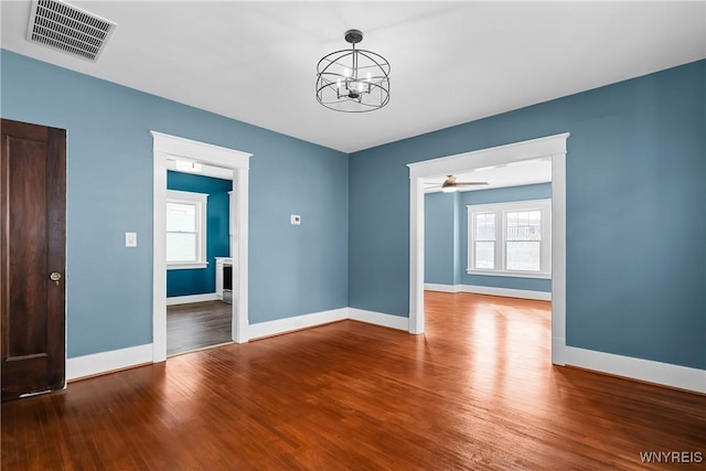 empty room featuring ceiling fan with notable chandelier and hardwood / wood-style floors