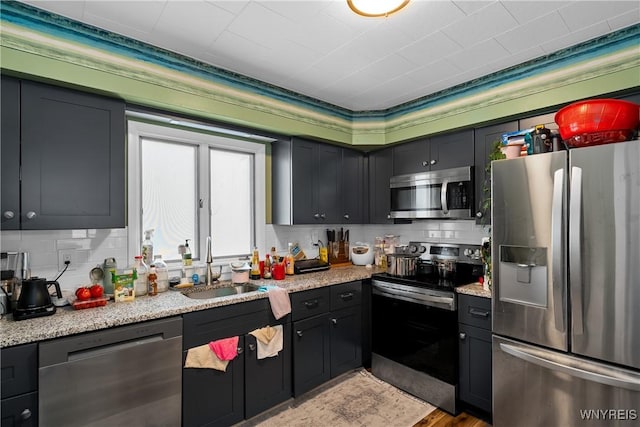 kitchen with light stone counters, sink, backsplash, and appliances with stainless steel finishes