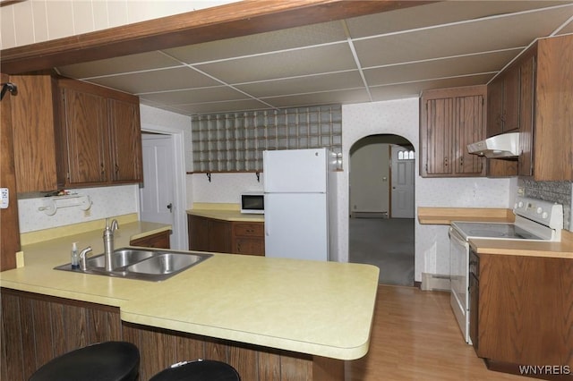 kitchen with sink, a breakfast bar area, a paneled ceiling, kitchen peninsula, and white appliances