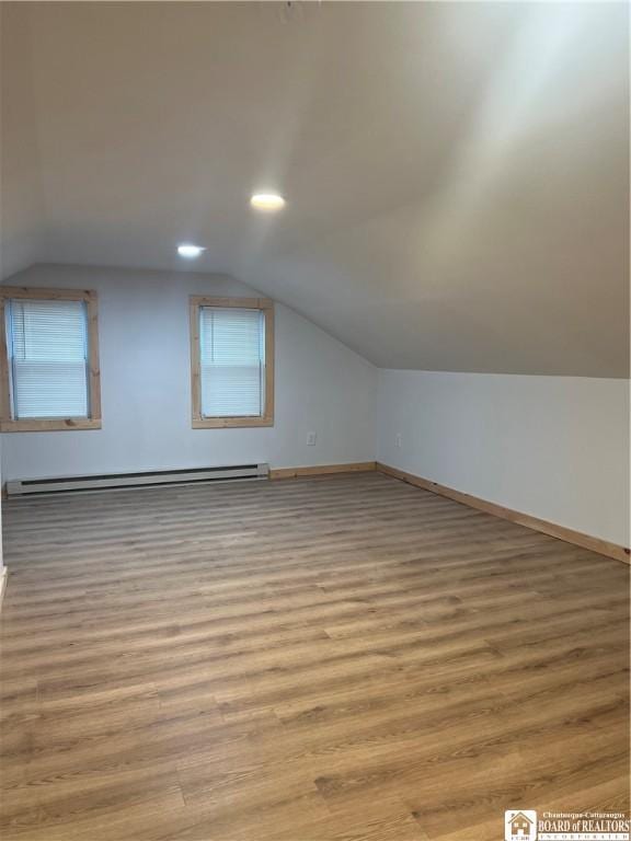 additional living space with a baseboard radiator, vaulted ceiling, and light hardwood / wood-style flooring