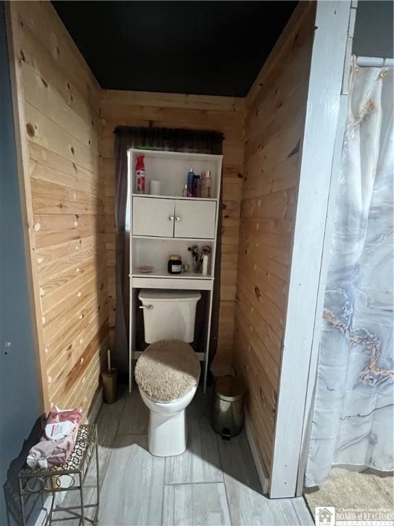 bathroom with a shower with curtain, toilet, and wood walls