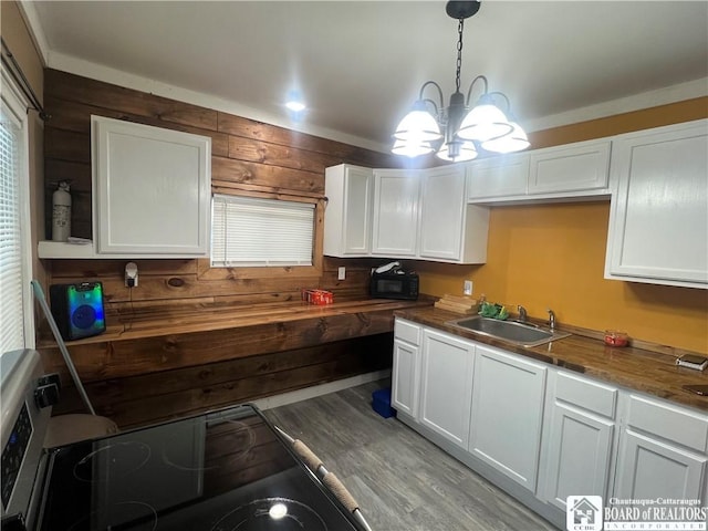 kitchen featuring white cabinetry, sink, pendant lighting, and wooden walls