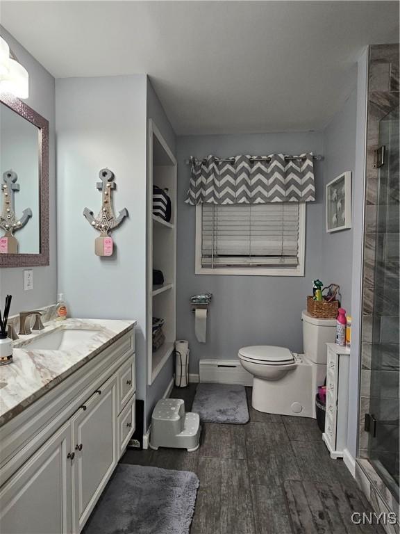 bathroom with a baseboard radiator, wood-type flooring, vanity, toilet, and a shower with door