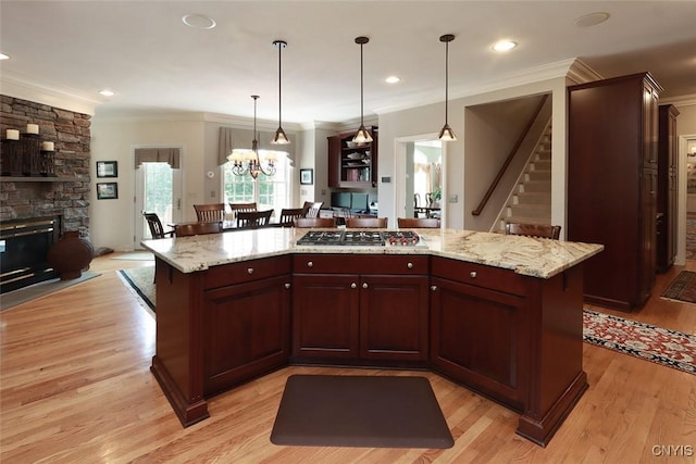 kitchen featuring pendant lighting, light hardwood / wood-style flooring, a center island, light stone countertops, and stainless steel gas stovetop