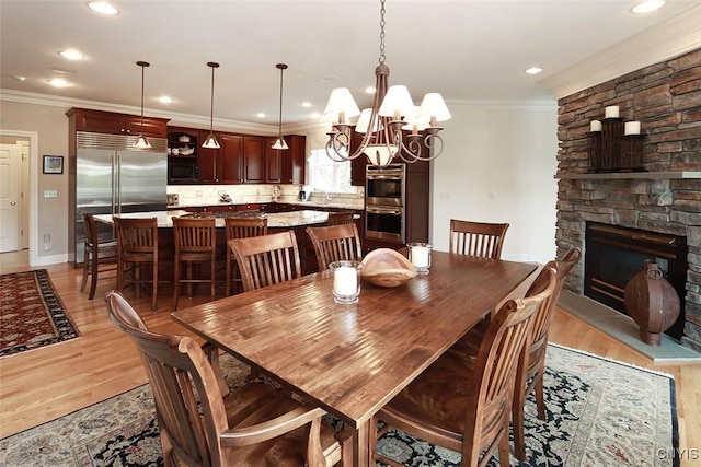 dining area featuring crown molding, a fireplace, a chandelier, and light hardwood / wood-style flooring