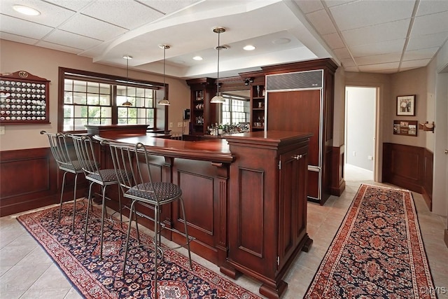 bar with a paneled ceiling, hanging light fixtures, a tray ceiling, paneled fridge, and wood walls