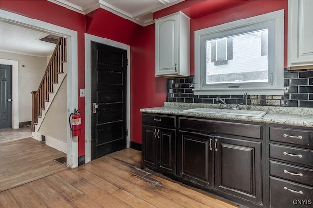 kitchen featuring tasteful backsplash, sink, white cabinets, ornamental molding, and light hardwood / wood-style flooring