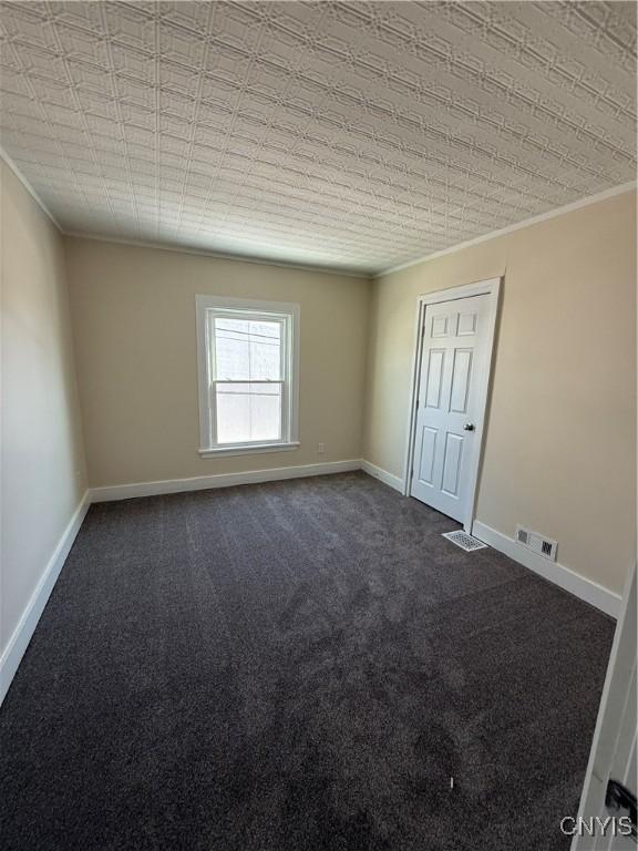 unfurnished room with ornamental molding and dark colored carpet