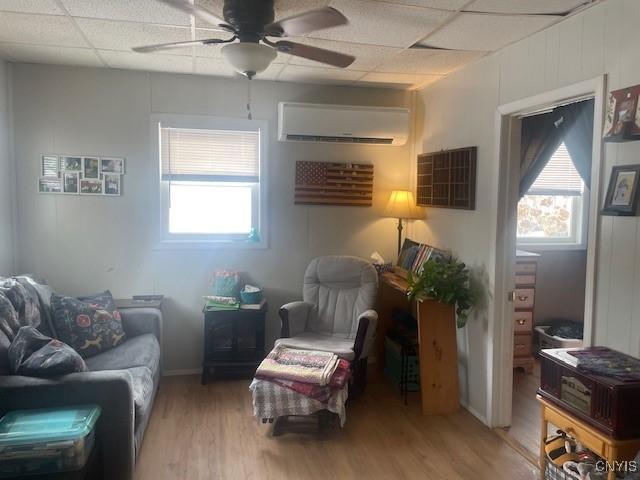 sitting room with a healthy amount of sunlight, hardwood / wood-style flooring, a paneled ceiling, and a wall mounted AC