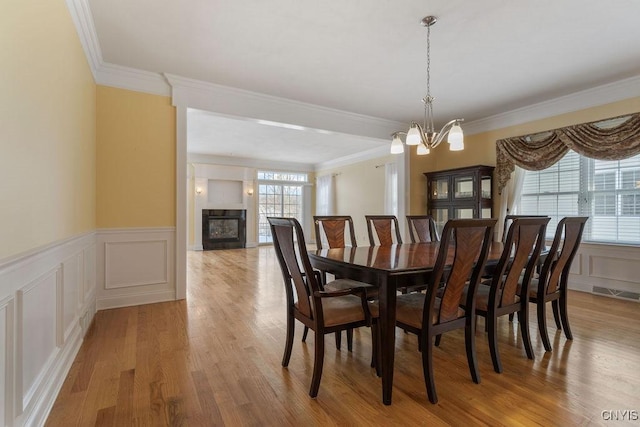 dining area with ornamental molding, a chandelier, light wood-type flooring, and a wealth of natural light