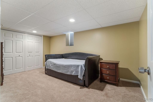 bedroom with light carpet, a paneled ceiling, and a closet