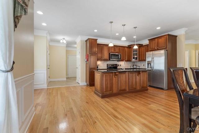 kitchen with light hardwood / wood-style flooring, ornamental molding, an island with sink, pendant lighting, and stainless steel appliances