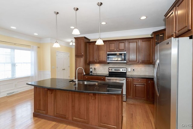 kitchen featuring sink, ornamental molding, appliances with stainless steel finishes, pendant lighting, and a kitchen island with sink