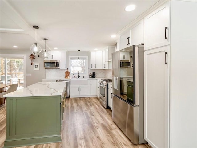 kitchen with a kitchen island, appliances with stainless steel finishes, decorative light fixtures, white cabinets, and light stone counters