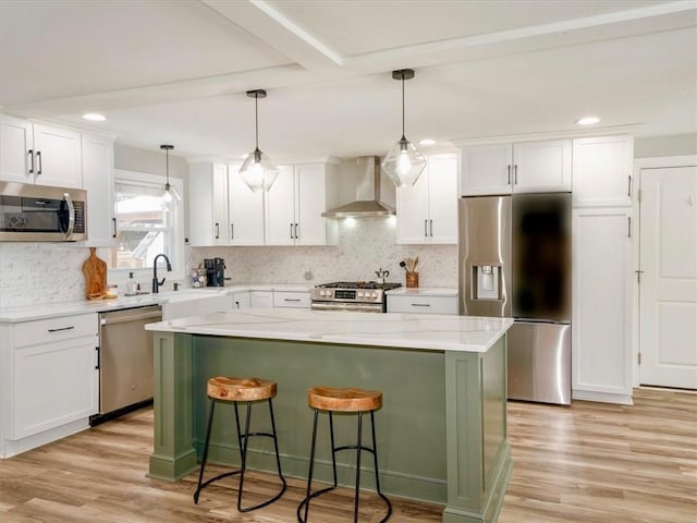 kitchen featuring decorative light fixtures, a center island, wall chimney range hood, stainless steel appliances, and white cabinets