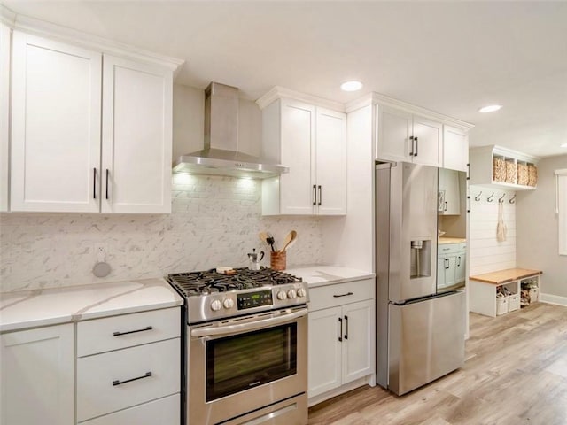 kitchen with wall chimney range hood, stainless steel appliances, white cabinets, and light wood-type flooring