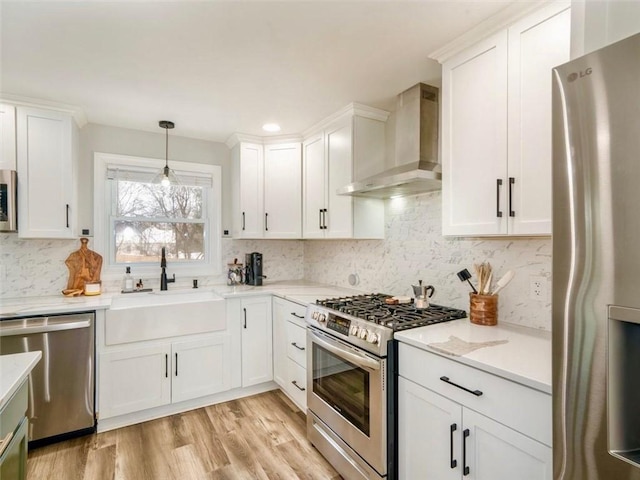 kitchen featuring sink, wall chimney range hood, stainless steel appliances, decorative backsplash, and white cabinets