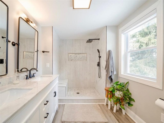 bathroom with wood-type flooring, tiled shower, a wealth of natural light, and vanity