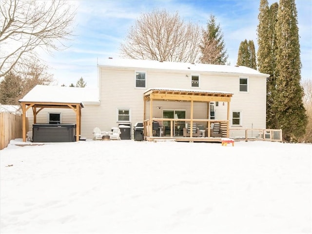 snow covered house featuring a wooden deck and a hot tub